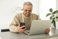 Concentrated senior man looking at laptop and phone calling at home. Royalty Free Stock Photo