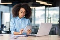 Concentrated and serious African American woman in blue shirt and glasses sitting in modern office at desk with laptop Royalty Free Stock Photo