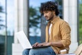 Concentrated and serious young Indian man using a laptop while sitting on a bench outside Royalty Free Stock Photo