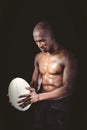 Concentrated shirtless athlete looking down while holding rugby ball