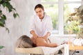 Skilled young masseuse doing back pain relief massage to elderly woman