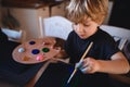 Concentrated small boy painting pictures indoors at home, leisure time.