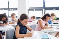 Concentrated small school children sitting at the desk in classroom, writing.