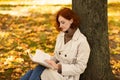 Concentrated smart caucasian millennial female with red hair in raincoat reads book and thinks