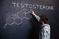 Concentrated student drawing chemical structure of testosterone molecule on blackboard