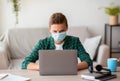 Concentrated teenager in face mask typing on laptop