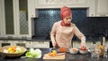 Woman in hijab stands at kitchen table cutting vegetable