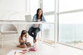 Concentrated woman write notes while her daughter sitting on floor. Royalty Free Stock Photo