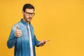 Confident young handsome man in casual working on laptop while standing against yellow background. Thumbs up Royalty Free Stock Photo