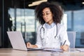Concentrated young African American female doctor, student practitioner studying and working online on laptop, sitting Royalty Free Stock Photo