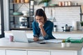 Concentrated young business woman using her mobile phone while working with computer in the kitchen at home Royalty Free Stock Photo