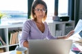 Concentrated young business woman working with computer while consulting some documents in the office at home Royalty Free Stock Photo