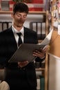 Concentrated young detective in black suit reading dossier in dark office. Investigator working with criminal case Royalty Free Stock Photo