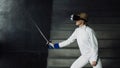 Concentrated fencer woman practice fencing exercises using VR headset and training simulator competition game indoors