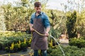 Young gardener in apron watering plants with sprinkler in garden Royalty Free Stock Photo