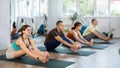 Concentrated young girl making stretching legs with group of active adult people sitting on yoga mat and doing exercise Royalty Free Stock Photo