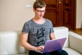 Concentrated young man with glasses working on a laptop in a home office. Type on a keyboard and scrolls text on the display Royalty Free Stock Photo