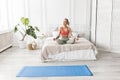 Concentrated young woman doing yoga, sitting in lotus pose on the bed. Beautiful blonde-hair girl in stylish sportswear Royalty Free Stock Photo