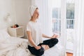 Concentrated young woman doing yoga, sitting in lotus pose on the bed. Wellbeing, healthy lifestyle concept Royalty Free Stock Photo