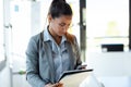 Concentrated young woman reading some documents while using smart phone in the office Royalty Free Stock Photo