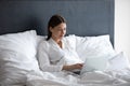 Focused young woman work on laptop lying in bed Royalty Free Stock Photo