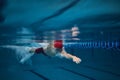 Concentration. Competitive young man, swimming athlete in goggles and red cap in motion, training in pool indoors. Royalty Free Stock Photo