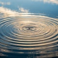 Concentric ripples form on a calm water surface, reflecting soft, golden clouds and blue sky. The Royalty Free Stock Photo