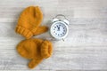 The concept of the arrival of cold winter days. Yellow warm mittens, white alarm clock on a gray background, top view, space for Royalty Free Stock Photo