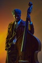 African-American man, elegant bassist in trendy hat engaged in music in neon light against gradient background.