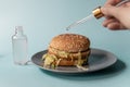 The concept of artificial enhancers of the taste of food. Pipette with flavor in hand over a hamburger
