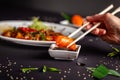 Concept of Asian cuisine. Girl is in Chinese or Japanese restaurant sushi, holds wooden sticks in her hands. Dunk sushi in sause Royalty Free Stock Photo