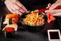 Concept of Asian cuisine. The girl is holding Japanese chopsticks in her hand and eating Chinese noodles from a black plate Royalty Free Stock Photo