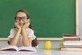 Concept back to school. Funny schoolgirl with glasses smiling while sitting at the table with books in the classroom. Royalty Free Stock Photo