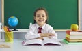 Concept back to school. Happy positive schoolgirl is smiling while sitting at the table on the background of the school