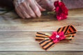Concept background of May 9 Russian holiday Victory Day. St. George`s ribbon on a wooden table, old woman holding in hands a red Royalty Free Stock Photo