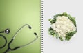 Concept of balanced medical diet with healthy food, paper notebook pages with stethoscope, and cauliflower isolated in white, copy