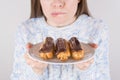 Concept of being on strict diet. Cropped close up photo of a human biting lower lip holding in hands white plate with yummy tarts