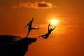 The concept of betrayal and the help of friends, Silhouette of Men are jumped between high cliff at a red sky sunset Royalty Free Stock Photo