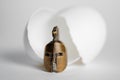 The concept of the birth of a warrior. Gladiator`s bronze helmet next to a broken egg shell on white background Royalty Free Stock Photo