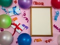 Wooden photo frame, multicolored streamer, gift boxes and balloons on a pink background.