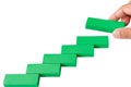 Concept of building success foundation. Hand put green puzzle wooden blocks in the shape of a staircase.