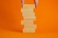 Concept of building success foundation. Men hand put wooden blocks on the stack of wooden blocks. Beautiful orange background,