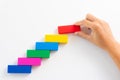 Concept of building success foundation. Women hand put red wooden block on colorful wooden blocks in the shape of a staircase. Royalty Free Stock Photo