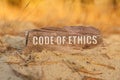 In the sand against the background of yellow grass there is a sign with the inscription - CODE OF ETHICS