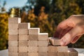 Concept of business promotion goals. Male fingers build stairs made of wooden blocks leading to the top. Blurry autumn background