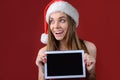 Concept of buying presents on Christmas holidays. Happy impressed woman in red dress and santa hat is holding digital tablet with Royalty Free Stock Photo