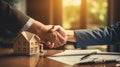 Concept of buying real estate. Handshake between the buyer and seller, with a miniature house and a contract in the background