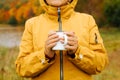 Concept for camping, travel, active retirement. Close-up of senior woman in yellow rain jacket holding iron mug hot drink Royalty Free Stock Photo