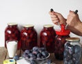 Concept of canning plum compote for future use in glass jars on a wooden table. Elderly woman`s hands seal the jar. Hobby of a Royalty Free Stock Photo