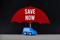 Concept of car insurance. Blue car under red umbrella with text Save Now
